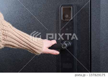 A woman opens a modern smart door lock with a digital keypad and biometric fingerprint access. A woman opens a modern smart door lock with a digital keypad and biometric fingerprint access. 137829175