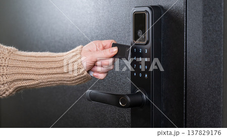 A woman opens a modern smart door lock using a contactless key. A woman opens a modern smart door lock using a contactless key. 137829176