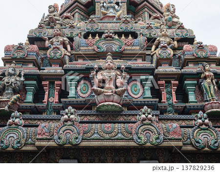 This image shows the vibrant, intricately carved gopuram of the Sri Maha Mariamman Temple. A central statue of Goddess Lakshmi is surrounded by tiered rows of deities and floral motifs, showcasing 137829236