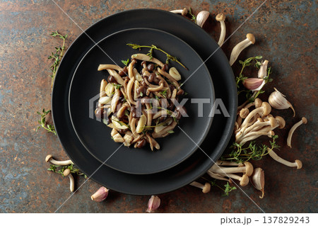 Fried shimeji mushrooms with thyme and garlic on a black plate. Fried shimeji mushrooms with thyme and garlic on a black plate. 137829243