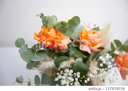 Elegant bouquet of orange roses with eucalyptus leaves placed in a decorative gift box on a white background. Celebration, appreciation, romance, floristry craft, and thoughtful present for special Elegant bouquet of orange roses with eucalyptus leaves placed in a decorative gift box on a white background. Celebration, appreciation, romance, floristry craft, and thoughtful present for special 137829356