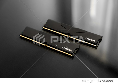 Black DDR5 RAM memory modules placed on a dark, glossy surface. RAM shortages on the market, rising prices, and increased demand driven by the growing need for AI training. Black DDR5 RAM memory modules placed on a dark, glossy surface. RAM shortages on the market, rising prices, and increased demand driven by the growing need for AI training. 137830991