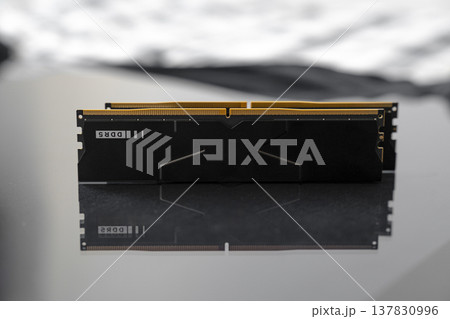 Black DDR5 RAM memory modules placed on a dark, glossy surface. RAM shortages on the market, rising prices, and increased demand driven by the growing need for AI training. Black DDR5 RAM memory modules placed on a dark, glossy surface. RAM shortages on the market, rising prices, and increased demand driven by the growing need for AI training. 137830996
