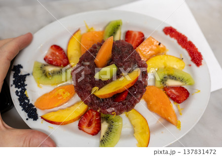 Red tuna tartare presented on a white plate, surrounded by fresh slices of kiwi, strawberries, peaches, and melon, garnished with black and red caviar Red tuna tartare presented on a white plate, surrounded by fresh slices of kiwi, strawberries, peaches, and melon, garnished with black and red caviar 137831472