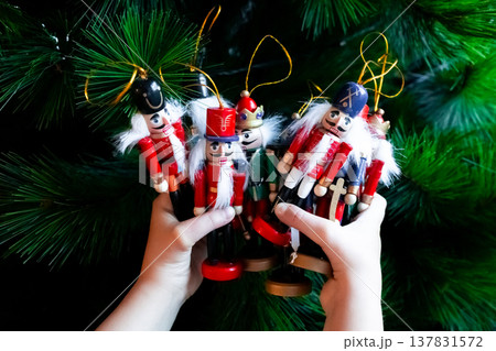 Child holding colorful wooden nutcracker ornaments against Christmas tree Child holding colorful wooden nutcracker ornaments against Christmas tree 137831572