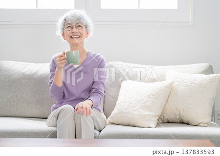 ソファーでコーヒーを飲みながらくつろぐシニア女性 ソファーでコーヒーを飲みながらくつろぐシニア女性 137833593