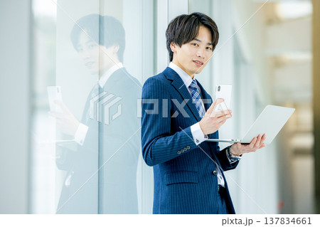 オフィスでノートパソコンを持って立っているスーツ姿の若いビジネスマン 137834661