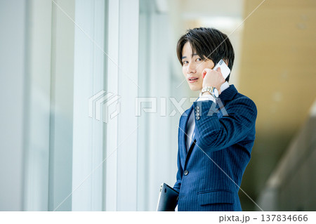 オフィスのロビーでスマホで通話する笑顔の若い男性 オフィスのロビーでスマホで通話する笑顔の若い男性 137834666