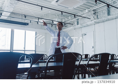白衣の男性医師が部屋で指差す 白衣の男性医師が部屋で指差す 137834910