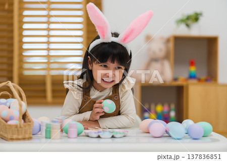 happy preschool child girl wearing bunny ears holding colorful egg while celebrating on easter day on table at home happy preschool child girl wearing bunny ears holding colorful egg while celebrating on easter day on table at home 137836851