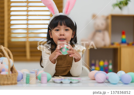 happy preschool child girl wearing bunny ears holding colorful egg while celebrating on easter day on table at home happy preschool child girl wearing bunny ears holding colorful egg while celebrating on easter day on table at home 137836852