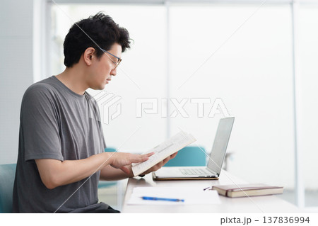 教室でPCや筆記用具を手元に置き書類を真剣に読む眼鏡をかけた30代の日本人の男性 137836994