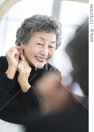 鏡を見ながらイヤリングをつける笑顔のシニア女性 鏡を見ながらイヤリングをつける笑顔のシニア女性 137837830