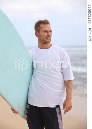 Surfer Holding Board. Portrait Of Male Surfer Holding Surfboard By Ocean Shore With Textured Fabric Background Surfer Holding Board. Portrait Of Male Surfer Holding Surfboard By Ocean Shore With Textured Fabric Background 137838040