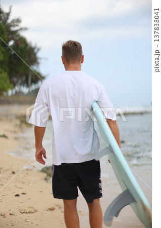 Casual Figure With Surfboard Under Arm Walking On Sand Along Coast Emphasizing Clothing And Product Display Casual Figure With Surfboard Under Arm Walking On Sand Along Coast Emphasizing Clothing And Product Display 137838041