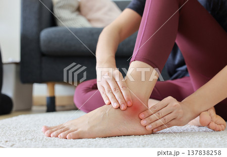 Woman massaging painful ankle and foot with red highlight. Ankle sprain, tendonitis, foot pain, gout and inflammation concept for health care, physical therapy and orthopedic medical treatment. Woman massaging painful ankle and foot with red highlight. Ankle sprain, tendonitis, foot pain, gout and inflammation concept for health care, physical therapy and orthopedic medical treatment. 137838258