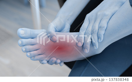 Woman sitting on floor and massaging her painful ankle with red highlight. Ankle sprain, joint inflammation, tendonitis and injury concept for health care, physical therapy and orthopedic treatment. Woman sitting on floor and massaging her painful ankle with red highlight. Ankle sprain, joint inflammation, tendonitis and injury concept for health care, physical therapy and orthopedic treatment. 137838348