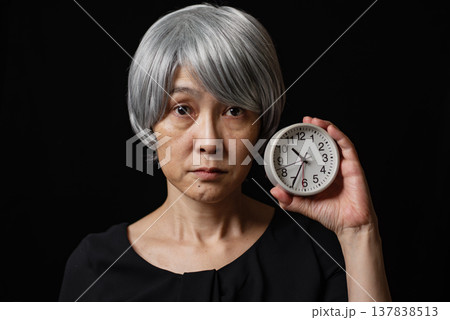 丸い時計を持ち無表情な白髪のシニア女性 137838513