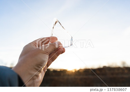Hand holding melting ice piece in sunlight symbolizing arrival of spring seasonal thaw and climate change Hand holding melting ice piece in sunlight symbolizing arrival of spring seasonal thaw and climate change 137838607