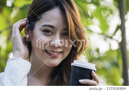 Woman drinking coffee hands holding hot disposable cup in green park. Happy Relax beautiful asian woman smiling face standing outdoors garden. Young women enjoy nature morning Freedom Lifestyle. 137838904