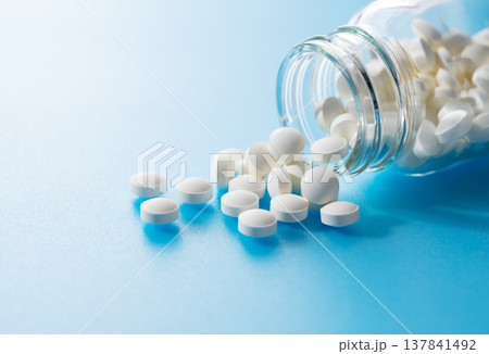 青い背景に置かれた瓶からこぼれ出た白い錠剤（サプリメント・薬） 137841492