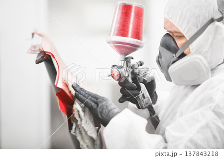Automobile repairman painter in mask and protective workwear painting car hood in paint chamber. Automobile repairman painter in mask and protective workwear painting car hood in paint chamber. 137843218