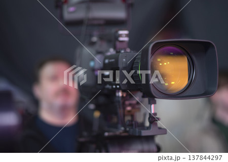 Professional broadcast camera in news studio with amber lens reflection and copy space Professional broadcast camera in news studio with amber lens reflection and copy space 137844297