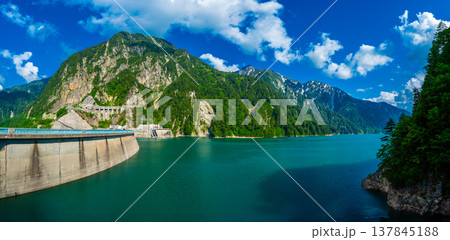 Panorama Beautiful scenery of Kurobe Dam on a brisk, with colorful lakeside mountains and crystal clear lake water under blue sunny sky in Tateyama Kurobe Alpine Route, Toyama, Japan 137845188