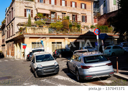 Cars parked on a quiet street near buildings with plants in an urban area at midday 137845371