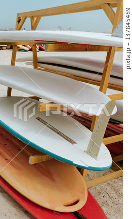 Surfboards stacked on a rack near a beach with people and water in the background Surfboards stacked on a rack near a beach with people and water in the background 137845489