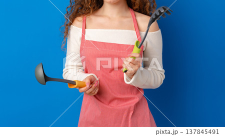 Woman holds kitchen and gardening tools with a blue background during day Woman holds kitchen and gardening tools with a blue background during day 137845491