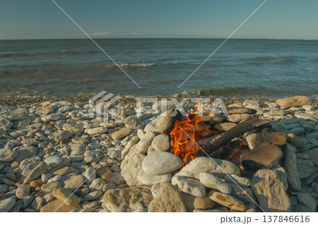 Warm Campfire in Stone Hearth on Pebble Beach at Sunset with Copy Space Warm Campfire in Stone Hearth on Pebble Beach at Sunset with Copy Space 137846616