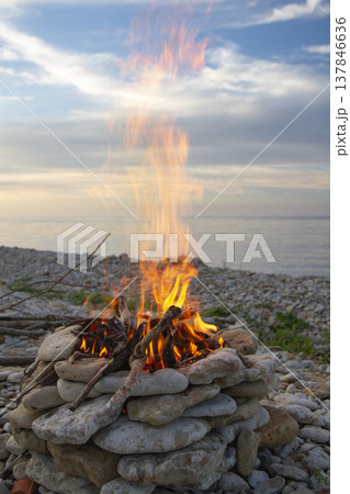 Vertical view of bright campfire burning on pebble beach by the sea with copy space Vertical view of bright campfire burning on pebble beach by the sea with copy space 137846636