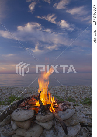 Vertical view of bright campfire burning on pebble beach by the sea with copy space 137846637