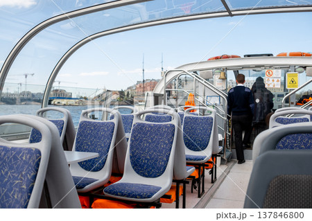 Passengers can enjoy the spacious interior of a stylish boat with ergonomic seating as crew members get ready to depart from the docks on a sunny day. Passengers can enjoy the spacious interior of a stylish boat with ergonomic seating as crew members get ready to depart from the docks on a sunny day. 137846800