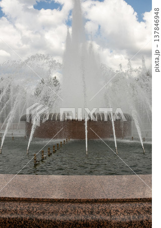 Water shoots into the air from a beautifully designed fountain surrounded by trees, inviting visitors to enjoy the refreshing atmosphere on a warm day. 137846948