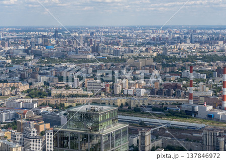 Vast expanse of Moscows urban landscape reveals buildings, greenery, and waterways under a blue sky with fluffy clouds, highlighting city life. 137846972