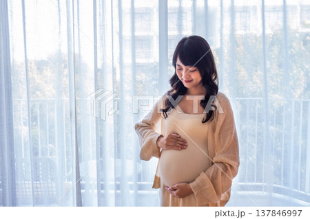 Pregnant woman standing with her hands gently rubbing her belly, showing love, warmth and concern for the baby with a happy smile. Pregnant woman standing with her hands gently rubbing her belly, showing love, warmth and concern for the baby with a happy smile. 137846997