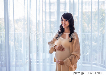 Pregnant woman standing with her hands gently rubbing her belly, showing love, warmth and concern for the baby with a happy smile. Pregnant woman standing with her hands gently rubbing her belly, showing love, warmth and concern for the baby with a happy smile. 137847000