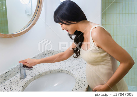Pregnant woman vomits in bathroom sink with mirror and light. Morning sickness from pregnancy. Pregnant woman vomits in bathroom sink with mirror and light. Morning sickness from pregnancy. 137847009