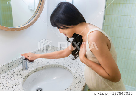 Pregnant woman vomits in bathroom sink with mirror and light. Morning sickness from pregnancy. 137847010