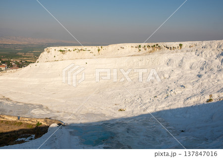 Visitors admire the white travertine terraces of Pamukkale in Turkey as the sun sets, highlighting the beauty and geological wonders of this unique location. 137847016