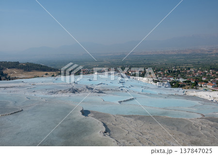 Pamukkale showcases its iconic white travertine formations as visitors admire the natural beauty against a clear sky in Turkey. 137847025