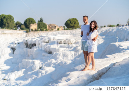 Visitors stand on the stunning travertine terraces of Pamukkale, soaking in the warm sunshine while overlooking the remarkable landscape. 137847125