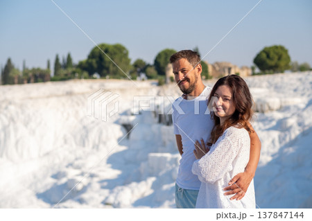 Beautiful couple stands together at Pamukkale, admiring the stunning white travertine terraces and warm thermal waters in a sunny, serene setting. Beautiful couple stands together at Pamukkale, admiring the stunning white travertine terraces and warm thermal waters in a sunny, serene setting. 137847144