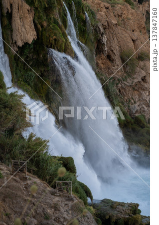 Water flows powerfully over rugged cliffs surrounded by lush greenery, capturing the beauty of nature at sunset in a tranquil setting. Water flows powerfully over rugged cliffs surrounded by lush greenery, capturing the beauty of nature at sunset in a tranquil setting. 137847160