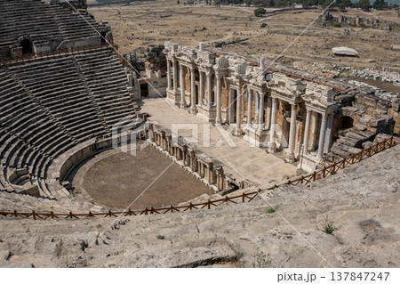 Tourists admire the well-preserved ruins of the ancient theater in Pamukkale, showcasing impressive columns and expansive seating in a historical context. Tourists admire the well-preserved ruins of the ancient theater in Pamukkale, showcasing impressive columns and expansive seating in a historical context. 137847247