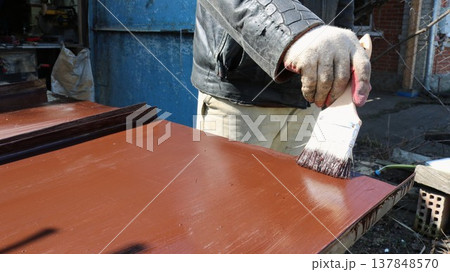 A painter covers a sheet of iron lying on the surface of a workbench with brown paint to prevent rust when using metal material in the household, applying protective paint to an iron product outdoors A painter covers a sheet of iron lying on the surface of a workbench with brown paint to prevent rust when using metal material in the household, applying protective paint to an iron product outdoors 137848570