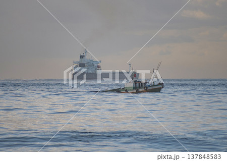 Small Fishing Boat and Large Cargo Ship in the Open Sea with Sky Copy Space 137848583