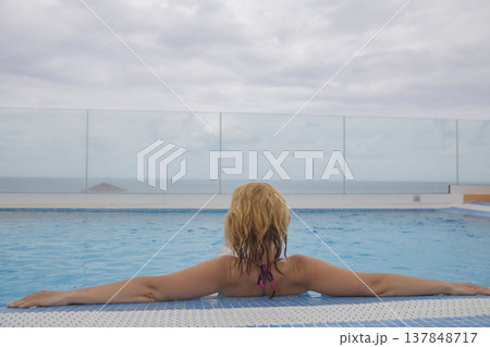 Relaxed woman in infinity swimming pool looking at ocean view with copy space in sky Relaxed woman in infinity swimming pool looking at ocean view with copy space in sky 137848717